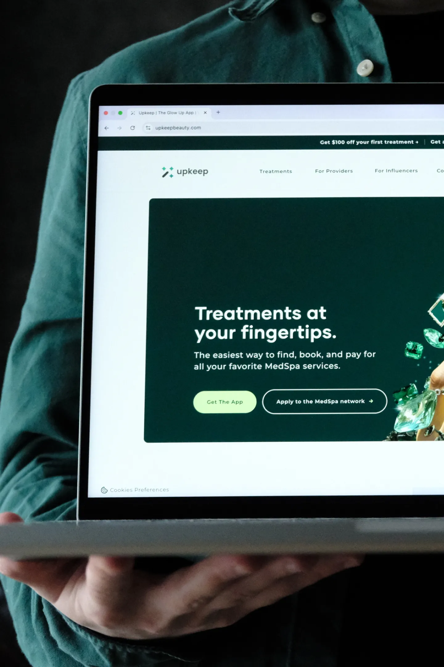 Person in green shirt holding a laptop showing Upkeep app for booking MedSpa treatments.